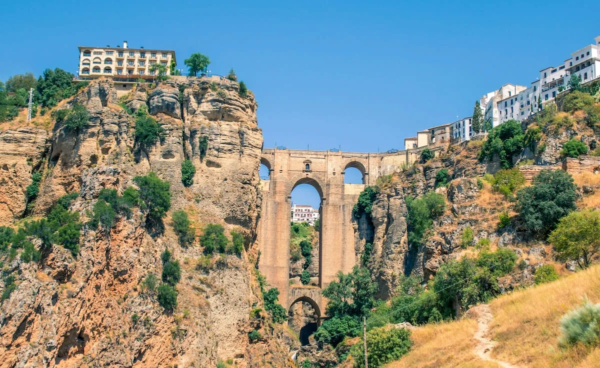 El Puente Nuevo visto desde abajo, entre los acantilados del Tajo, con un sendero en primer plano